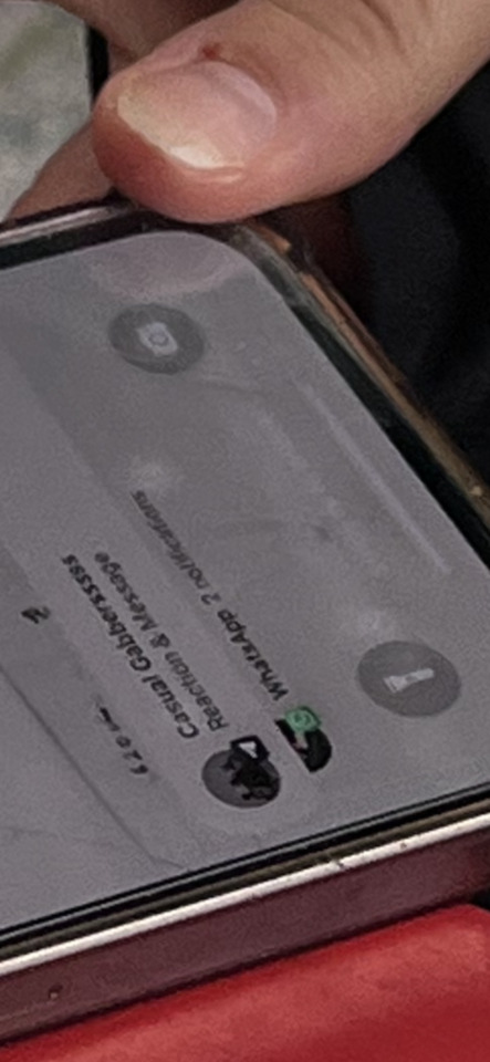 A finger hovers over a smartphone screen displaying WhatsApp and other notifications in dim light.