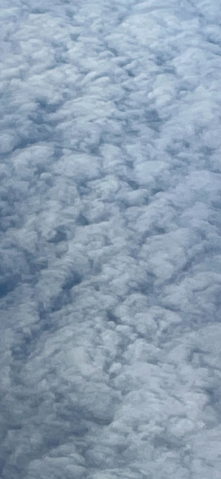 An aerial view of a vast, textured blanket of white and grey clouds stretching to the horizon.