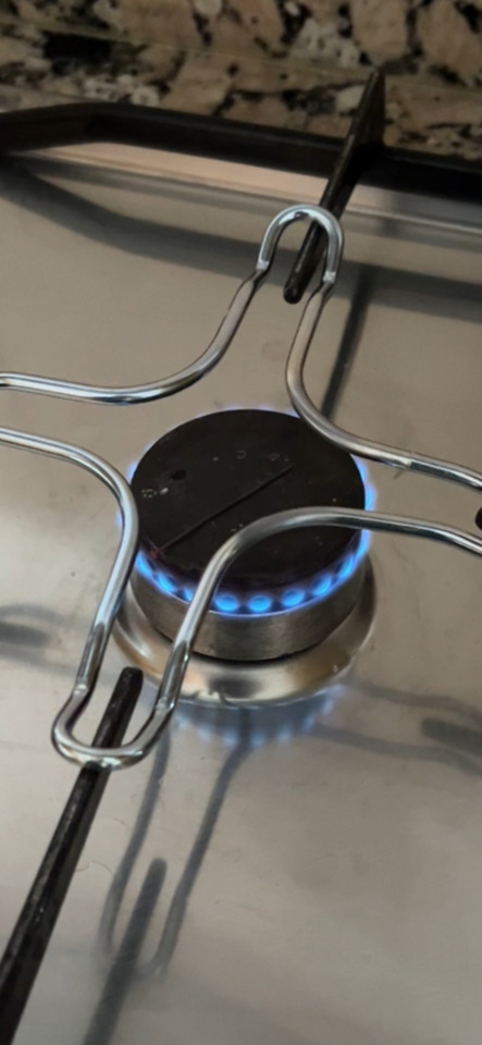 A close-up shot of a gas stove burner with a bright blue flame under shiny metal grates on a stainless steel surface.