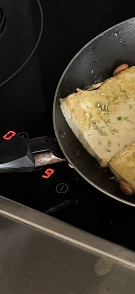 Close-up of golden toast with herbs cooking in a pan on a black induction stovetop with red digital displays.