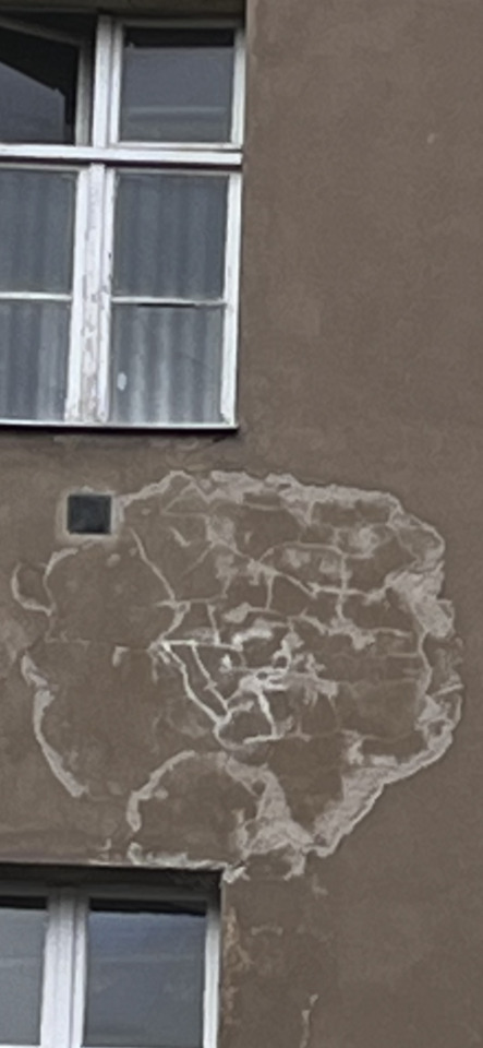 Close-up of a building facade with two windows, showing extensive peeling paint and a small dark square.