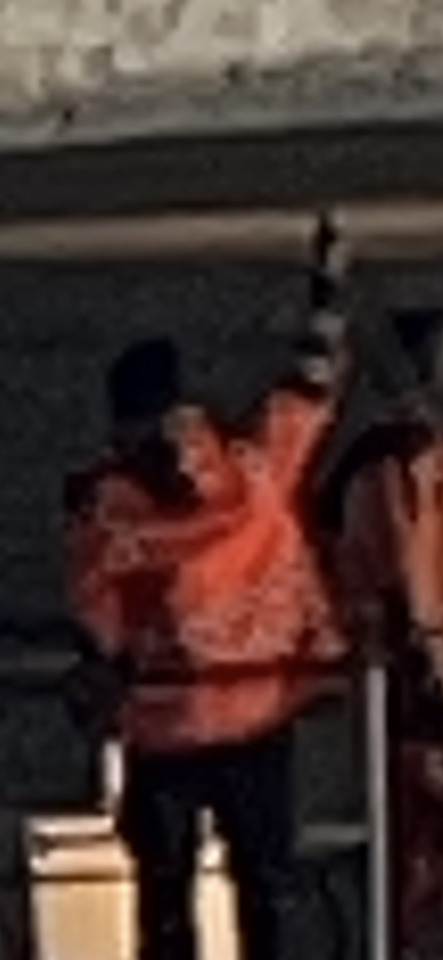 A blurry person in a bright orange jacket and dark pants stands in a dimly lit, dark environment.