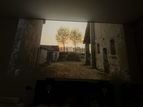 A projected image of a rustic farm scene at sunset, with old buildings and trees silhouetted against a warm sky.
