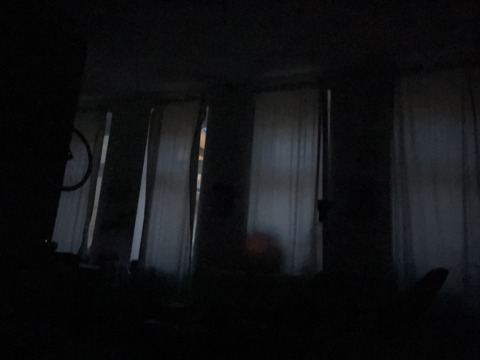 A dark room with three windows covered by sheer curtains, dimly lit by light filtering from outside.