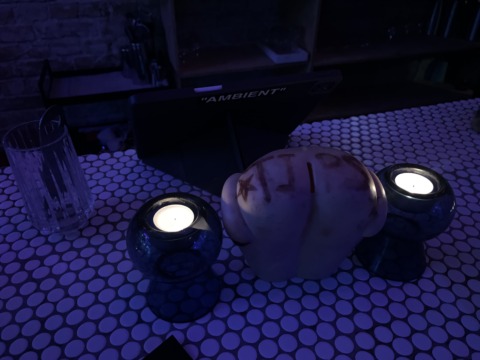 A dimly lit table with two flickering candles, a glass, and a decorative object on a polka-dot surface.