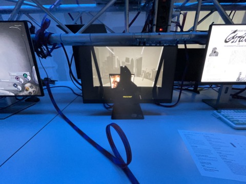 A desk with three computer monitors under blue lighting, showing a video game, a document, and a cityscape.